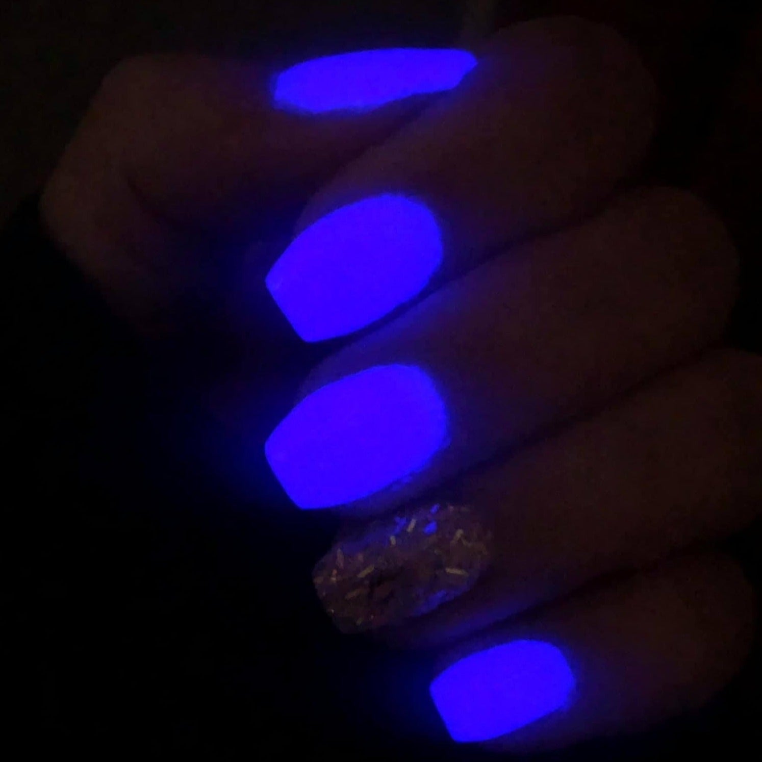 Purple glowing nails with one glittery gold accent nail under blacklight.