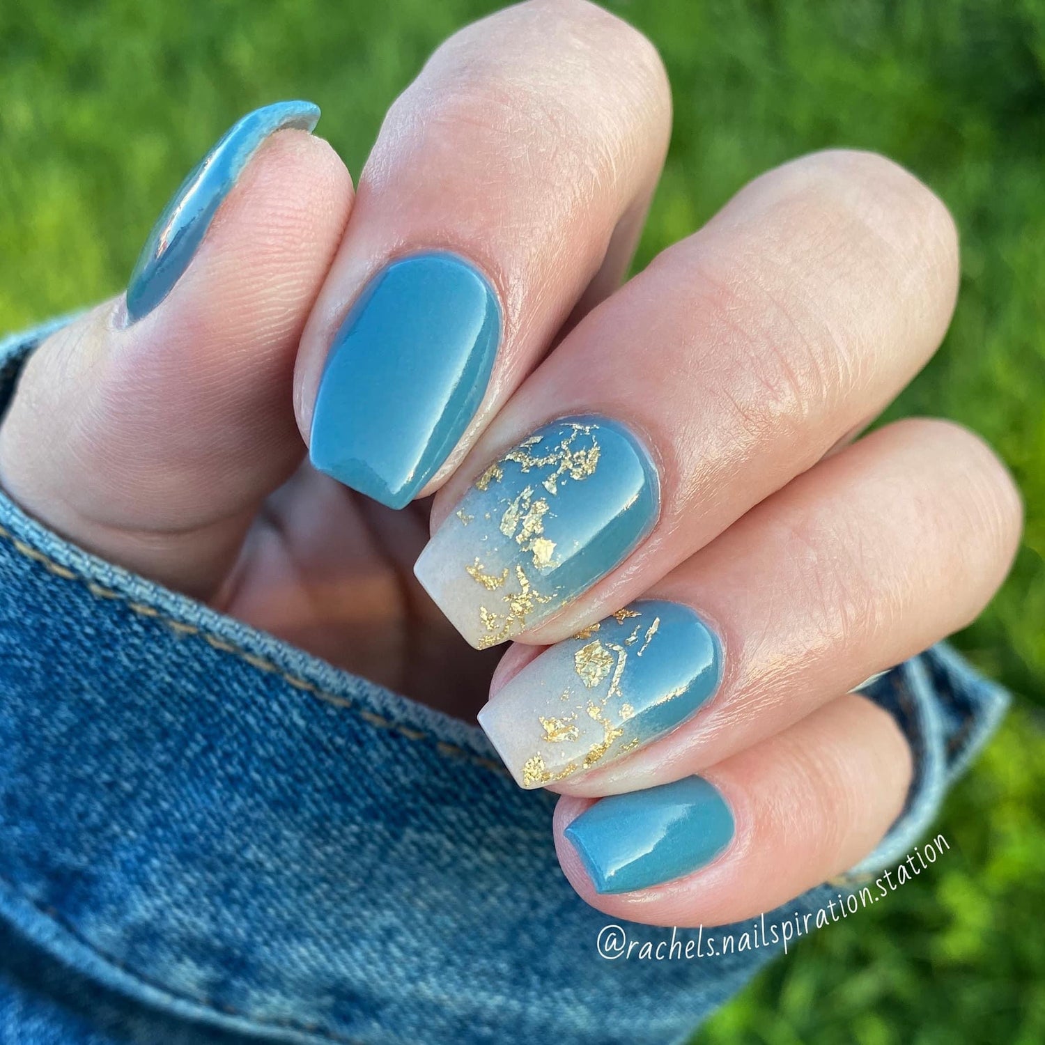 Hand with blue minimalist dip powder nails, one nail featuring clear polish with gold flakes accent.