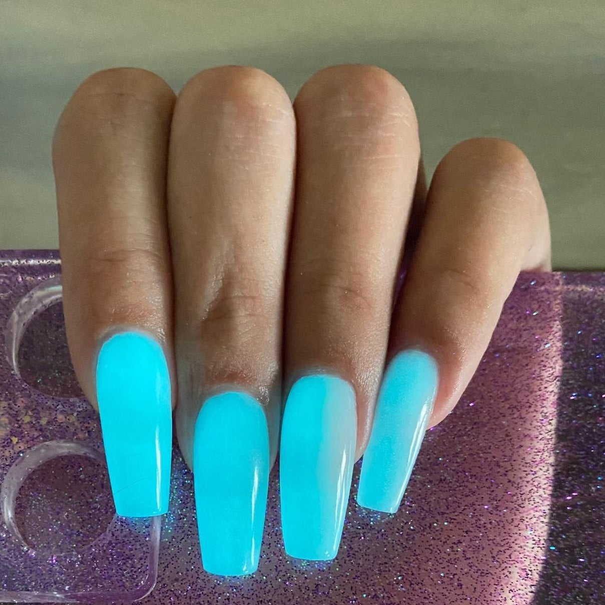 Long coffin-shaped nails with glossy blue glow-in-the-dark dip powder transitioning to milky white near the cuticles.