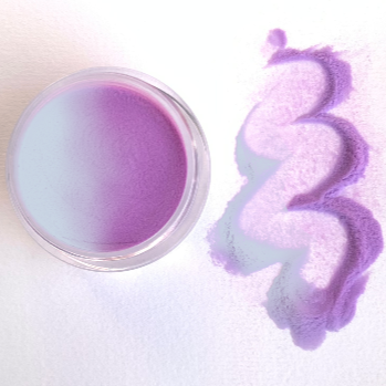 Round container of purple-to-blue color-changing dip powder with swirled purple powder trail on white background.